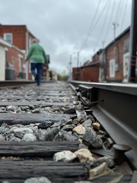 Person in green shirt and jeans walking on the railroad track while it rains in downtown Bremen